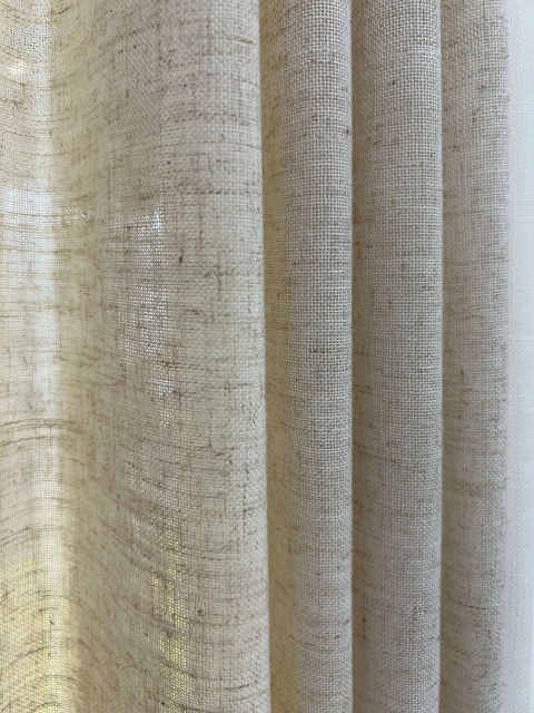 Textured linen-look drapery fabric close-up with neutral beige and taupe woven texture and soft vertical folds