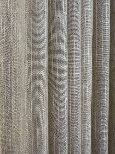 Close-up detail of natural beige linen-look drapery fabric with woven texture, subtle vertical stripe effect, and soft vertical folds